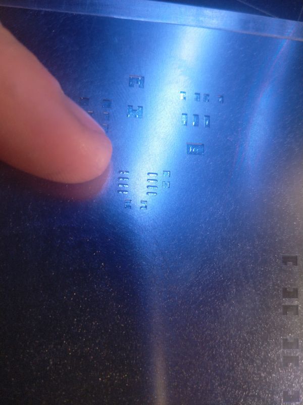 A metal stencil with several holes, touched by a finger.