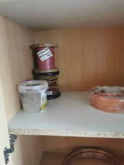 Półka z szpulami przewodów i plastikowym pojemnikiem wewnątrz szafki.