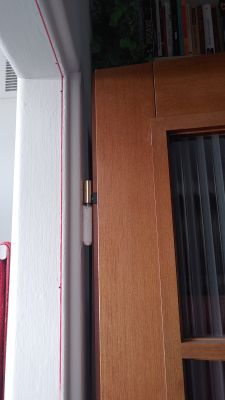 Zbliżenie na zawias drzwi drewnianych przy białej ościeżnicy z czerwoną linią zaznaczenia