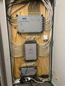 Szafa telekomunikacyjna z urządzeniami Telmor i siecią kabli.