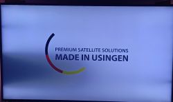 Ekran telewizora z zacienieniem po lewej stronie i widocznym logo PREMIUM SATELLITE SOLUTIONS MADE IN USINGEN.