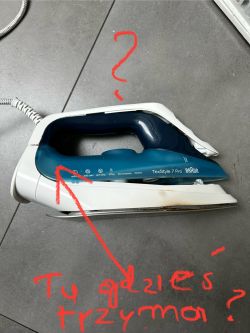 Żelazko Braun TexStyle 7 Pro leżące na podłodze z zaznaczonymi pytaniami o ukryte śruby.