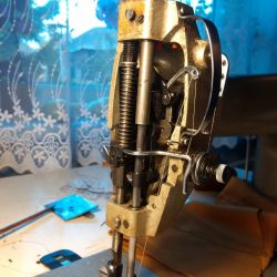 Maszyna do szycia z widocznymi częściami mechanicznymi i górnym nawlekaczem.