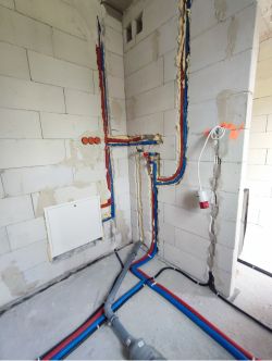 Instalacja hydrauliczna w ścianie z rurami PEX czerwonymi i niebieskimi oraz trójnikiem.