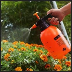 Person using an orange pressure sprayer on flowers in a garden.