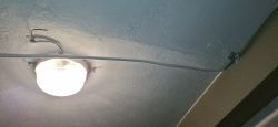 Kabel elektryczny biegnący pod sufitem piwnicy z przymocowaną lampą.