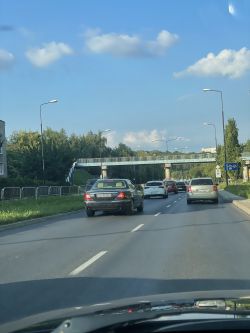 Widok z samochodu na ulicę z ruchem w godzinach szczytu, z widocznymi tablicami rejestracyjnymi kilku pojazdów.