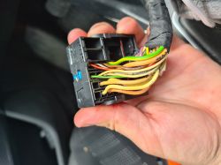 Electrical connector with colorful wires held in hand, seen inside a car.