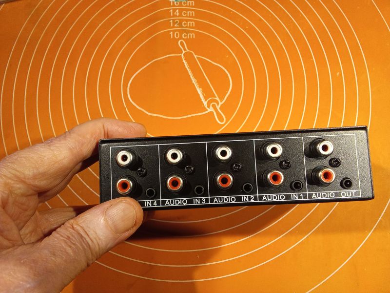 Selekor audio z czterema wejściami RCA i jednym wyjściem w trzymaniu dłoni.