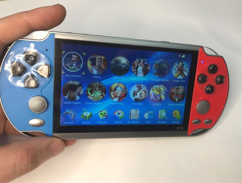 X12 handheld game console in a hand, showing a game menu on the screen, blue and red casing