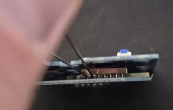 Flashing BSEED E-Series Board Without Soldering Close-up of a circuit board with two sewing needles inserted between its layers.