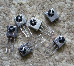 Several metal infrared receivers with three pins lying on a carpet.