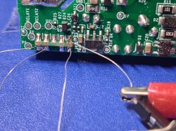 Close-up of a PCB with soldered wires and a red alligator clip on a blue work mat