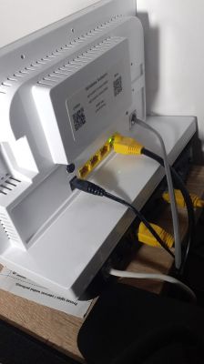 Domowy router z podłączonymi kablami Ethernet i zasilania, ustawiony na półce.