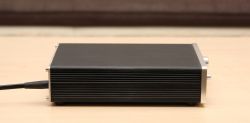 Black Headphone Amplifier on a Table Black headphone amplifier with a visible power cord, placed on a table.