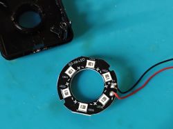 A round PCB with six SMD LEDs and two attached wires, lying on a blue surface.