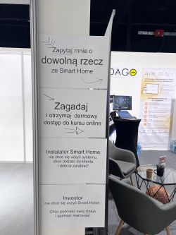 Trade booth banner in Polish about Smart Home; nearby a small table, armchairs, and a monitor stand.