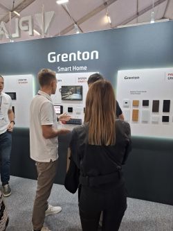 Stoisko Grenton Smart Home z panelami i ekranem, kilka osób rozmawia o systemie inteligentnego domu