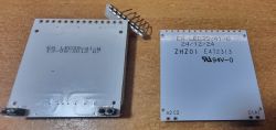 Dwa białe podświetlacze LED wyświetlacza EA LED39x41, leżące na brązowym blacie, z jednym pin-headerem u góry.