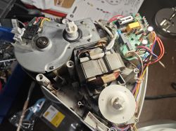 Inside of a device showing motor, gearbox housing, and a PCB with capacitors and multicolored wires