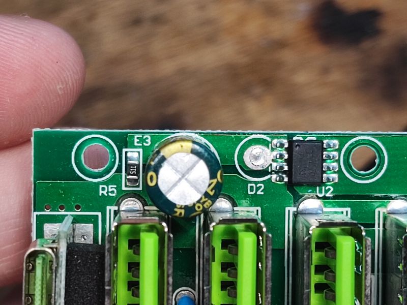 Zbliżenie na fragment płytki drukowanej z zielonymi portami USB, kondensatorem elektrolitycznym i układami SMD.