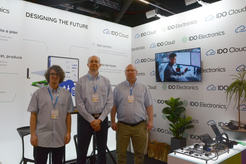 Stoisko IDO Electronics na targach z trzema pracownikami przed oznakowaniem firmy.