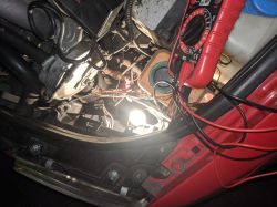 Zdjęcie przedstawia wnętrze maski samochodu z widocznym okablowaniem i miernikiem elektrycznym.