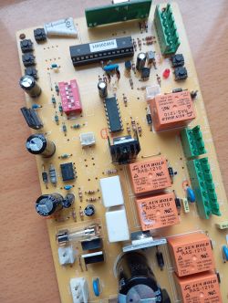 Zbliżenie na płytkę obwodu drukowanego z różnymi komponentami elektronicznymi, w tym przekaźnikami i kondensatorami.