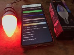Controlling a Tuya LED bulb after firmware modification A red-glowing LED bulb next to a smartphone showing a lighting control web interface.