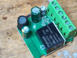 Moduł SB490 z zielonymi złączami i czarnym przekaźnikiem na drewnianym tle