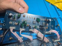 Dłoń trzyma płytkę PCB z elementami elektronicznymi i białymi taśmami przewodów na niebieskiej macie
