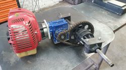 Brushcutter engine connected to a blue gearbox and chain drive mechanism