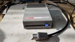 Prototype Atari XF351 Disk Drive View of a prototype Atari XF351 disk drive with SIO cable on a white surface.