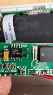 Close-up of a green PCB with an IC, SMD parts, and a ribbon cable in the background