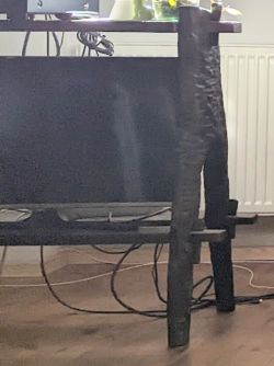 Zbliżenie na bok drewnianego stolika RTV z telewizorem i przewodami, na tle grzejnika