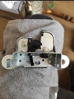 Zamek klapy bagażnika z mechanizmem i mikro stykami na szarej tkaninie.