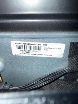 Barcode label on a metal device housing with visible cables.