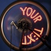 Bicycle wheel lit with red LED dot text, with wires and electronics mounted on the spokes
