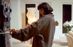 Person in a gray coat operates a reel-to-reel tape recorder in a modern living room