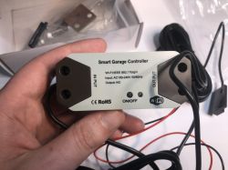 Smart Garage Controller with Wi-Fi and Cable Set A Smart Garage Controller held in hand, showing input/output ports, ON/OFF button, and cables.