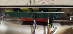 Bottom view of a green PCB with a connected multicolored wire bundle inside a metal enclosure