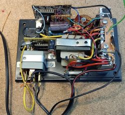Otwarta obudowa z układem elektronicznym: transformator, kondensatory i okablowanie na płycie montażowej