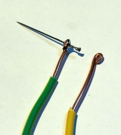 Close-up of two copper wires with green and yellow insulation, with curved ends.