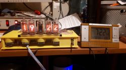 Nixie clock na biurku obok cyfrowego zegara.