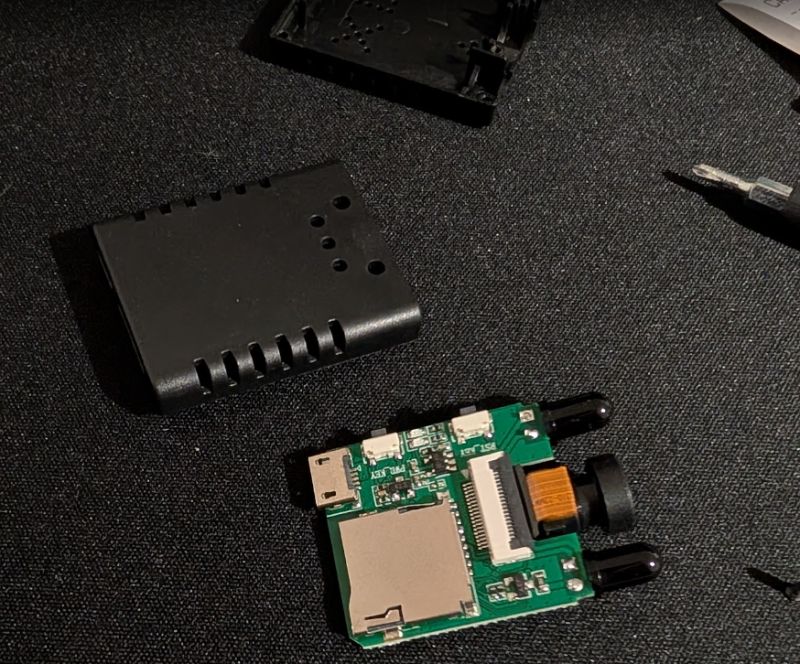 Disassembled small camera with PCB and plastic housing on dark fabric