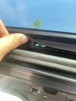 Osoba trzymająca uszczelkę przykręconej szyby samochodowej, odsłaniając śrubkę i powiększony otwór montażowy.