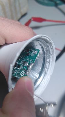 Person holding a circuit board inside a white cylindrical casing.
