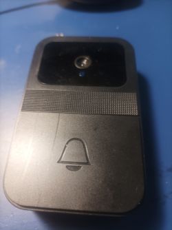 Video doorbell with camera on blue surface Black video doorbell with camera and bell symbol button, resting on a blue surface.