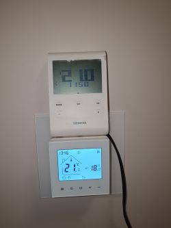Two thermostats on a wall: a modern touchscreen unit and an older Siemens model.
