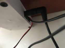 Close-up of power cables connected to a white enclosure under a shelf, showing a DC Jack connector and wires powering an LED strip.